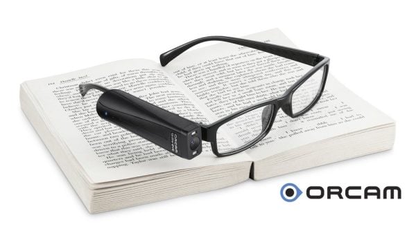 Image of Orcam MyEye on a pair of glasses resting on a book.