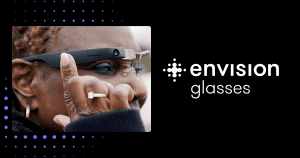 A woman is outdoors and wearing Envision glasses. Her fingers is on the side of the frame, navigating through the options. The text reads: Envision Glasses.