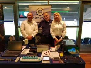 Photo of three Sight and Sound Technology staff standing behind a table with a number of products on it.